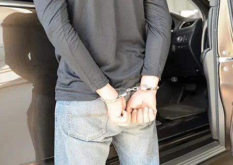 A man in handcuffs is standing next to a car.